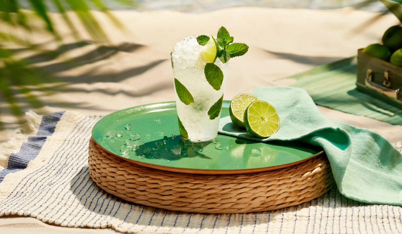 Mojito cocktail with mint, lime wedge, placed near cut limes and linen napkin.