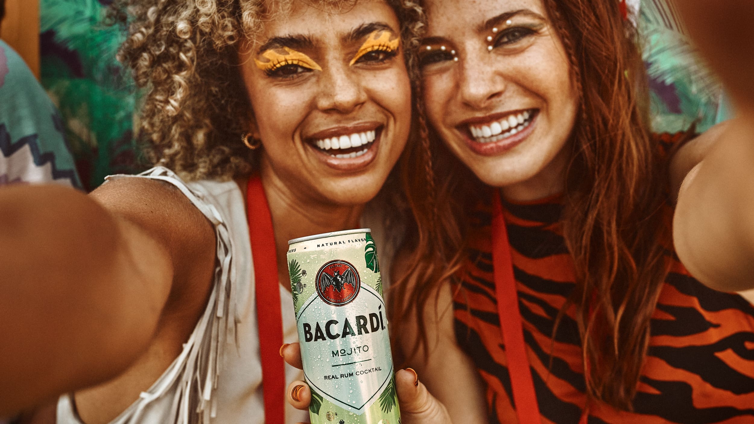 Two people taking a selfie at an outdoor event, one holding a Bacardí Mojito can.