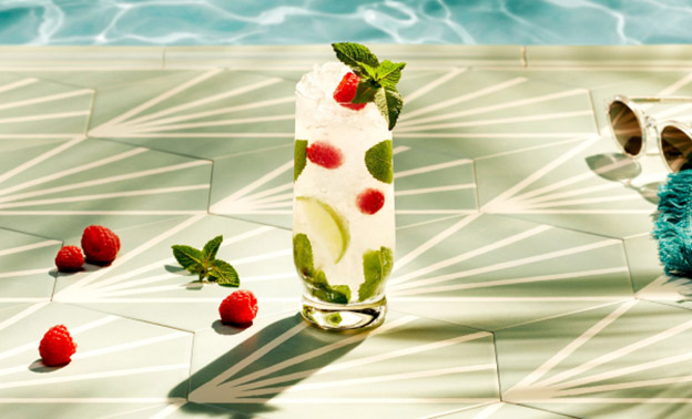 Raspberry mojito cocktail garnished with mint, raspberries, lime slice near pool.