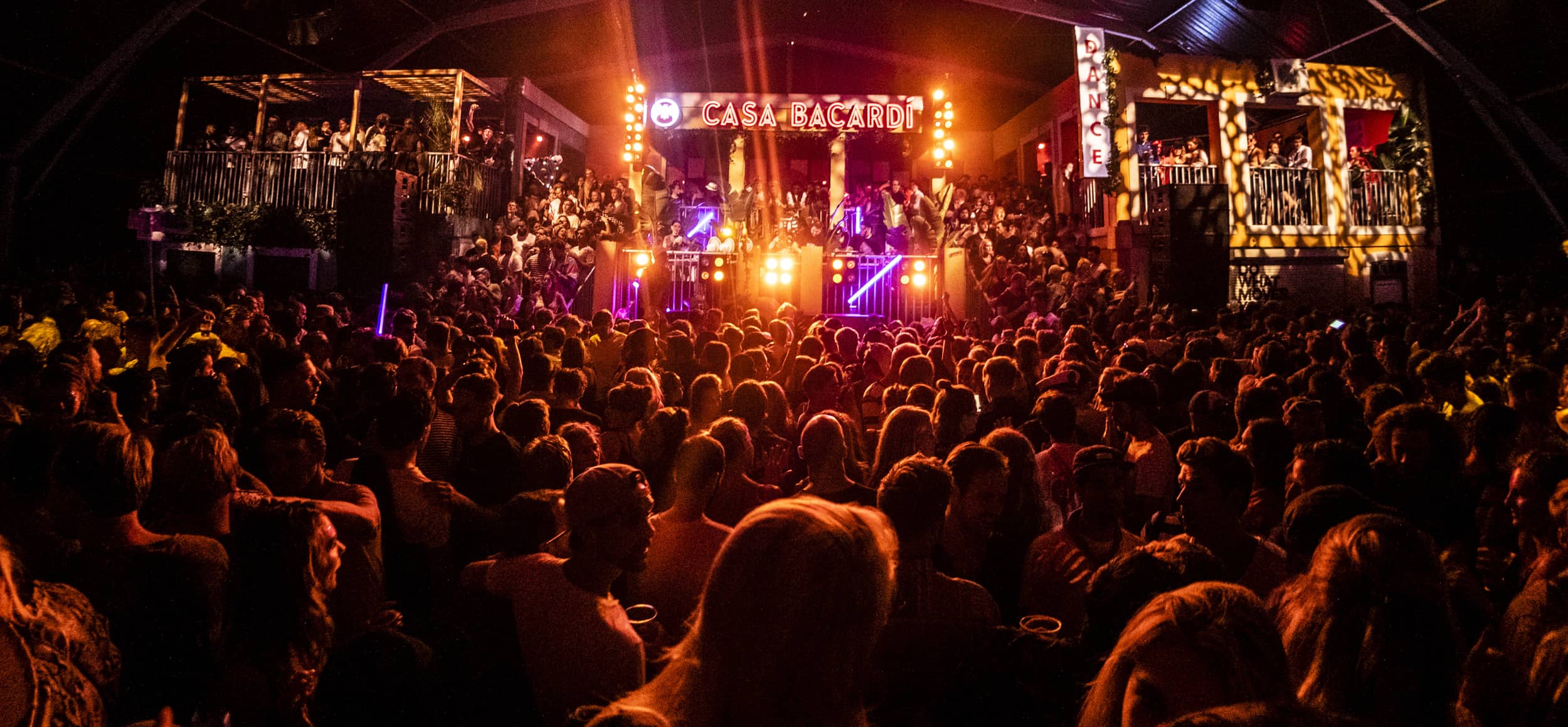 Large crowd at an indoor music event with Casa BACARDÍ sign, illuminated by orange and purple stage lights.