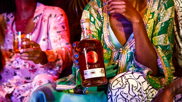BACARDÍ Reserva Ocho rum bottle held during social gathering with cocktail glasses.