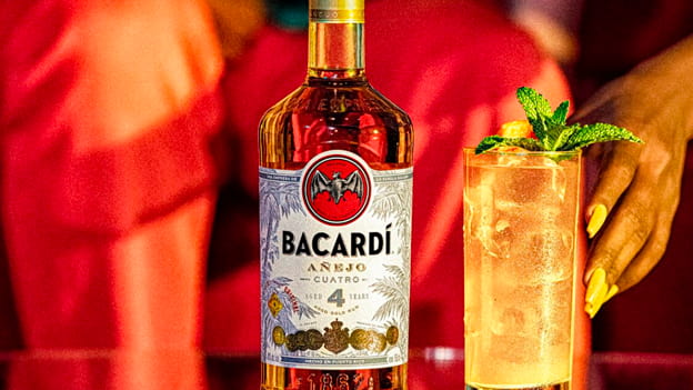 BACARDÍ Añejo Cuatro rum bottle beside cocktail with mint, garnished with citrus.