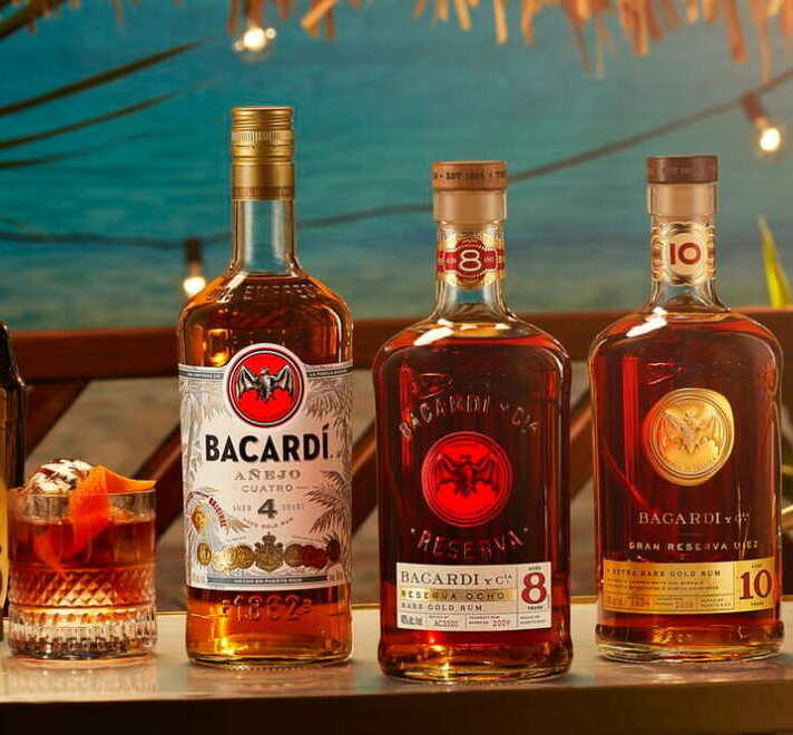 Three BACARDÍ rum bottles arranged next to a cocktail glass with an orange peel garnish.