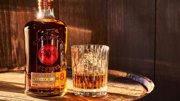 Bacardí Reserva Ocho rum bottle and crystal glass with ice cubes placed on a wooden surface.