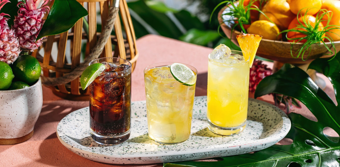 Three cocktails on a tray with lime wedge, pineapple garnish, and varied colors of drinks.
