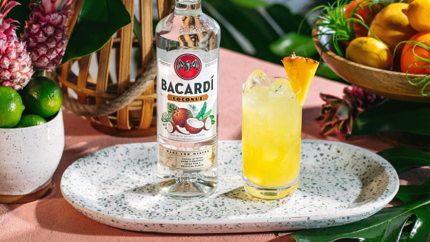 BACARDÍ Coconut rum bottle beside yellow cocktail with pineapple wedge and ice.