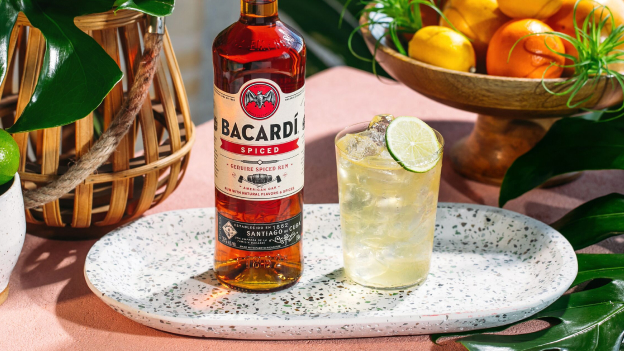 BACARDÍ Spiced Rum bottle next to cocktail with lime slice and ice.