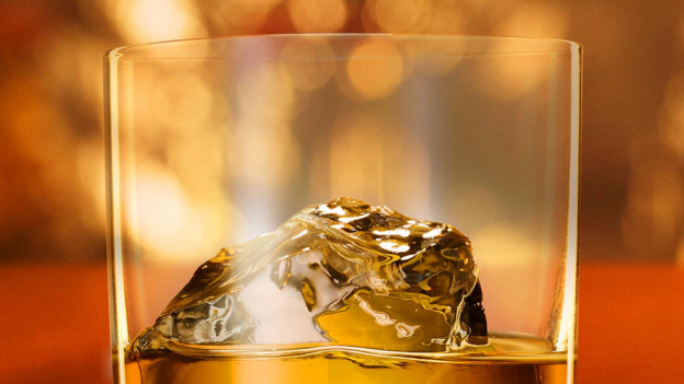 Close-up of amber liquid cocktail with large ice cube in a glass.