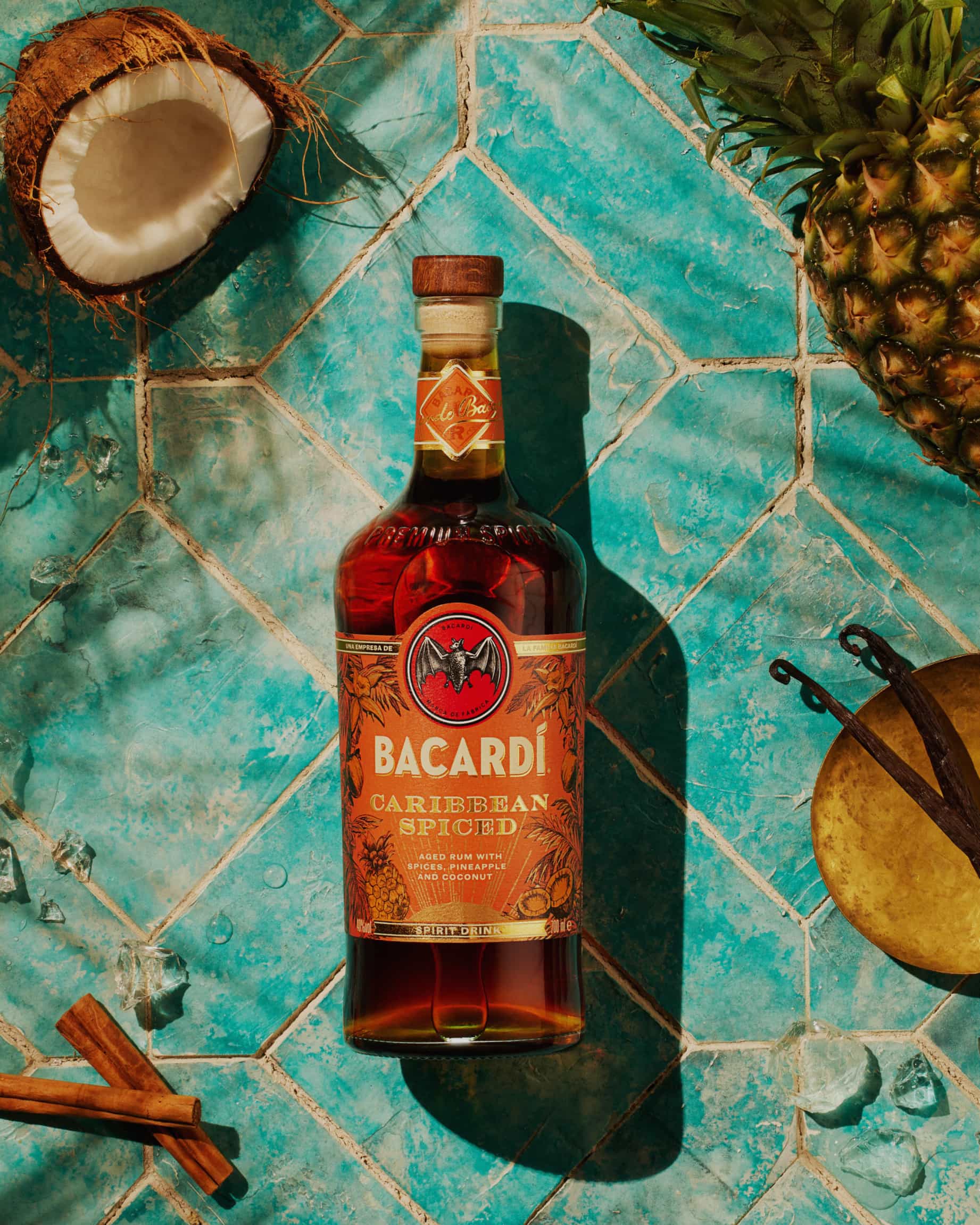 BACARDÍ Caribbean Spiced rum bottle surrounded by coconut, pineapple, cinnamon sticks, vanilla pods.