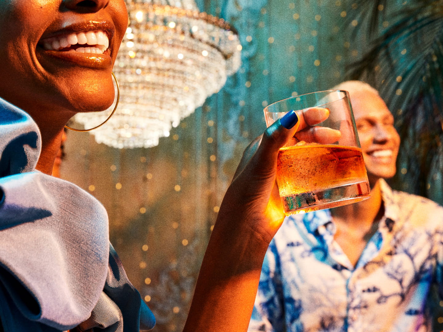 Person holding a drink at a social gathering with another person visible in the background.