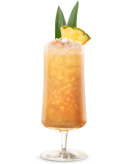Tall glass with golden-orange cocktail, pineapple wedge, green leaves, crushed ice, frothy top with reddish spice.