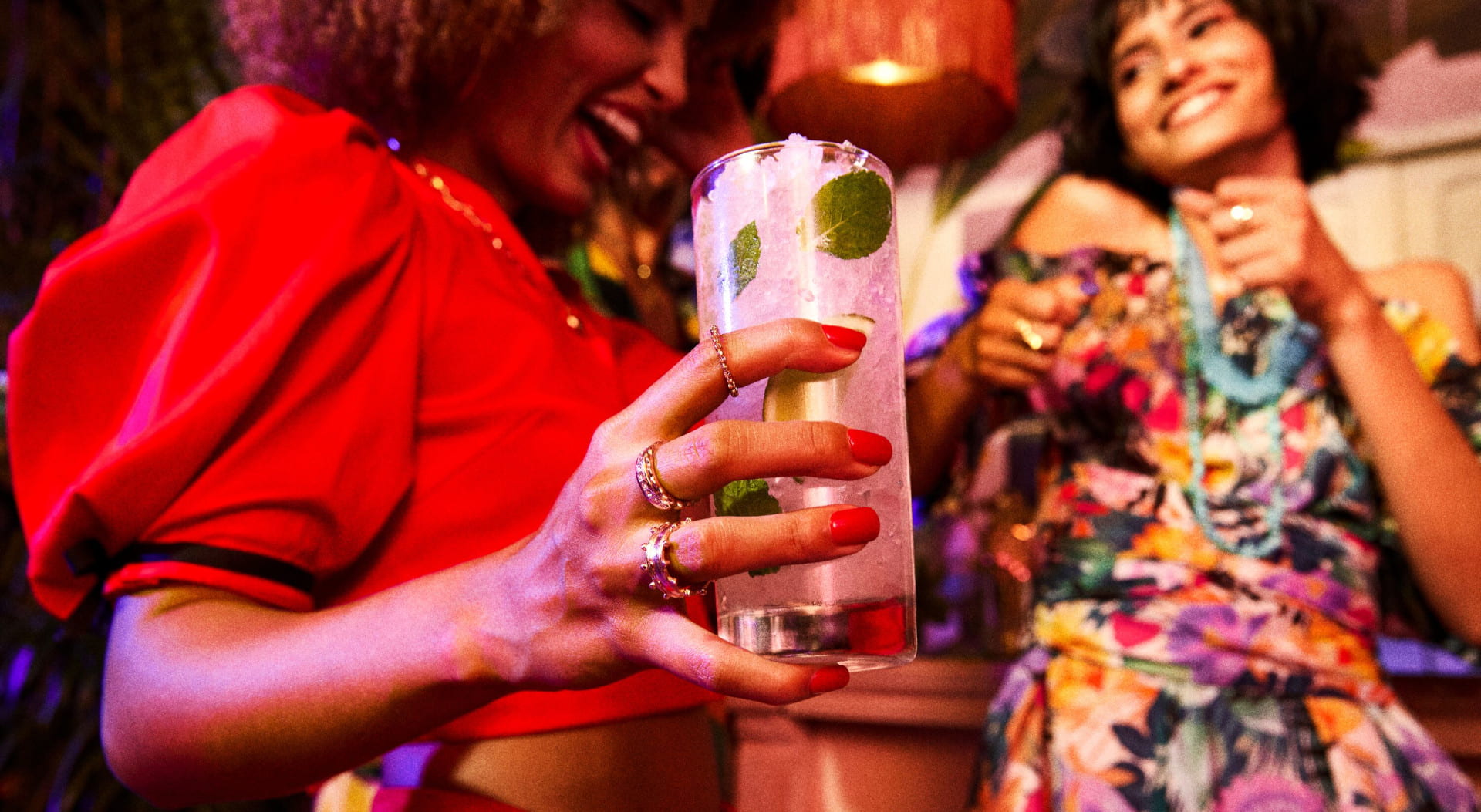 Person holding a tall cocktail glass with mint leaves, ice, and a clear drink.
