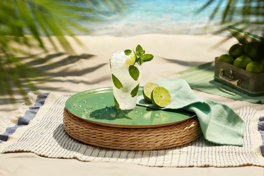 Mojito cocktail on a woven tray with lime and mint garnishes.