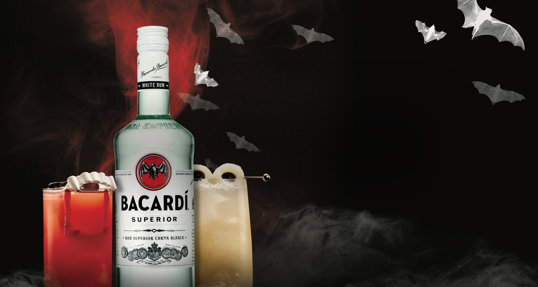 BACARDÍ Superior white rum bottle beside two Halloween cocktails with vampire teeth and ring garnishes.