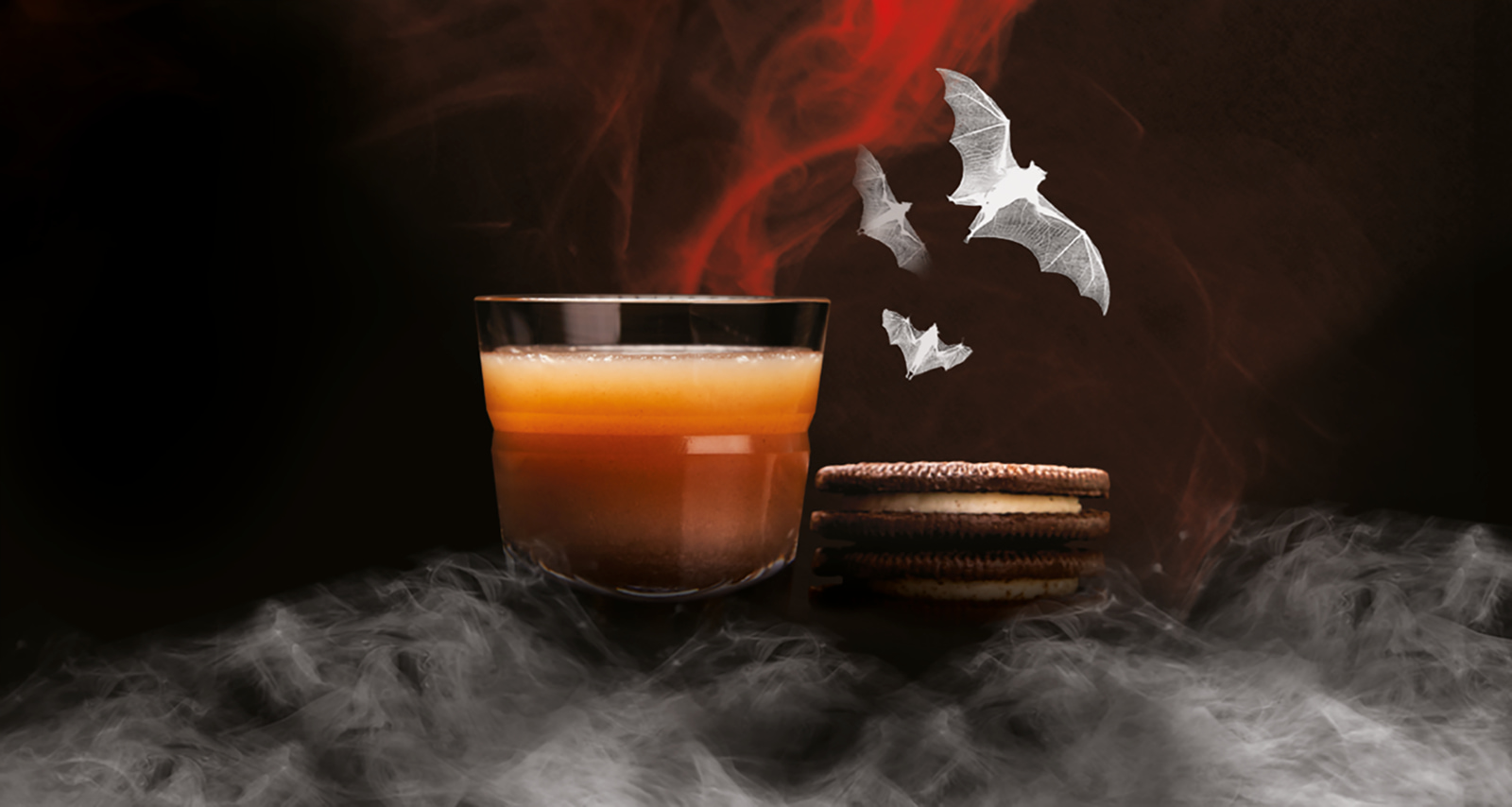 Halloween cocktail with orange and yellow layers next to a stack of cookies, surrounded by bats.
