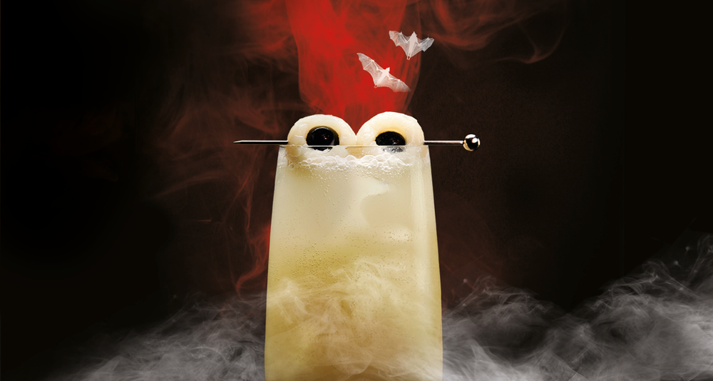 Halloween cocktail with lychee and cherry 'eyes' on skewer, accompanied by small bat cutouts.