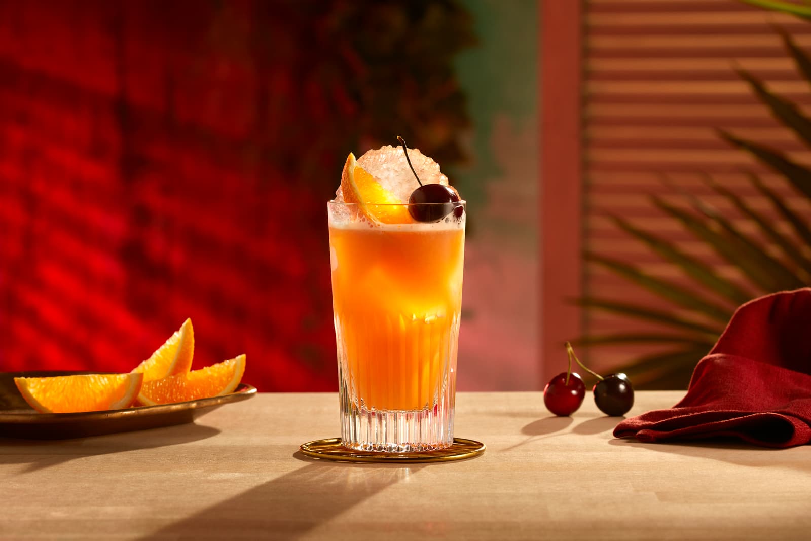 Orange cocktail in a tall fluted glass with crushed ice, orange slice, and cherry.