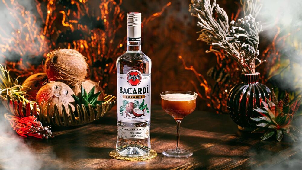 BACARDÍ Coconut rum bottle next to a dark cocktail in a coupe glass with coconuts.