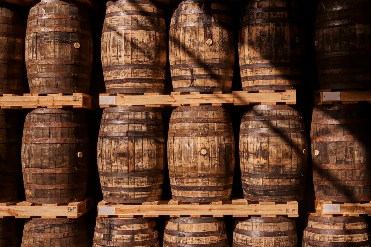 Close-up of aged wooden barrels with rusty metal bands on wooden pallets.