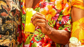 Hand holding tall glass of bright yellow cocktail with pineapple garnish.