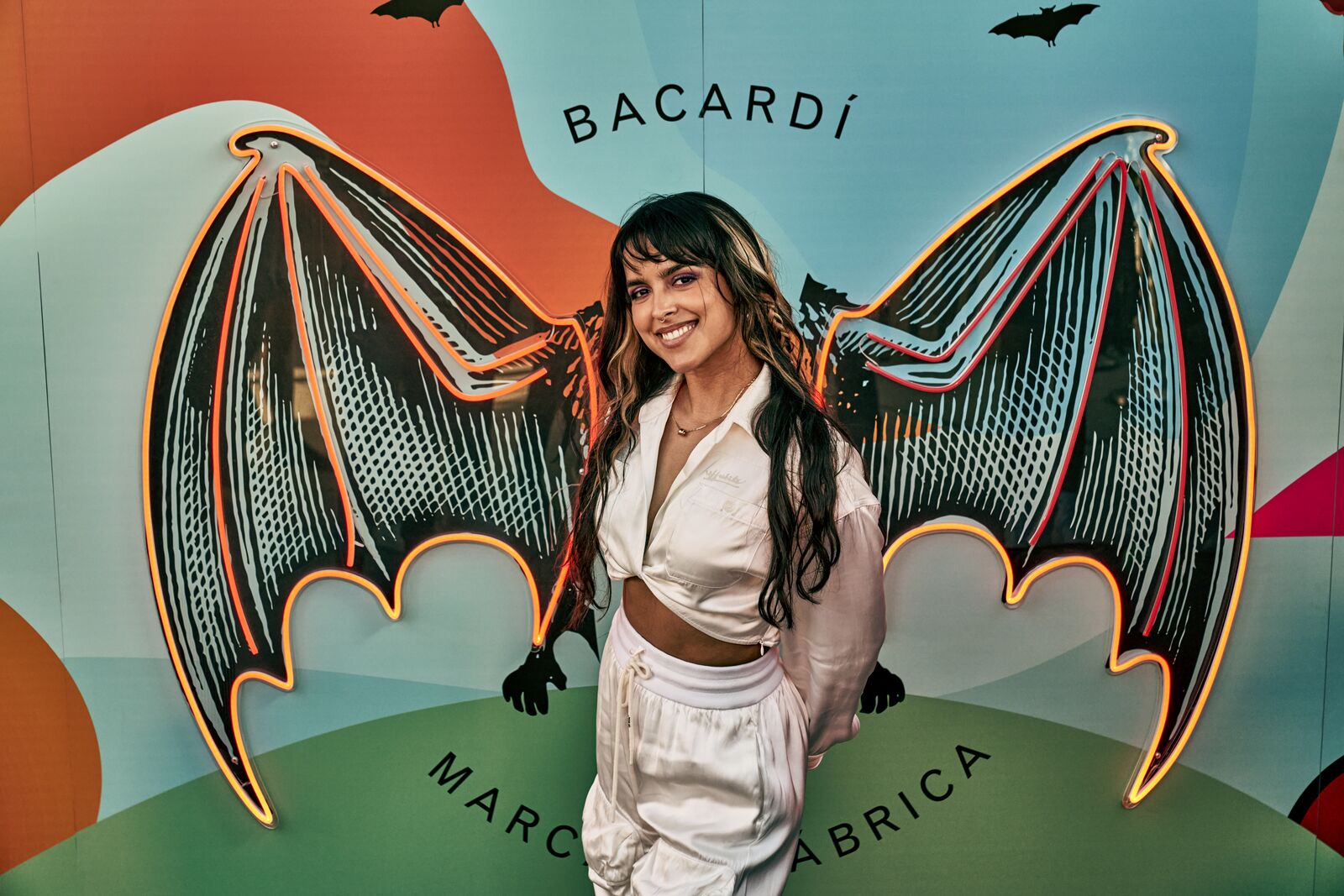 Woman standing in front of a vibrant BACARDÍ branded backdrop with illuminated bat wings.