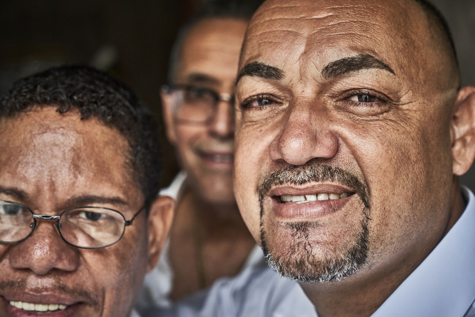 Three individuals smiling in a close-up group portrait, with one person prominently in focus.