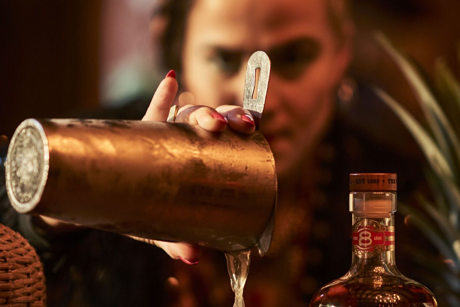 Hand pouring liquid from a copper cocktail shaker with a BACARDÍ 8 bottle nearby.