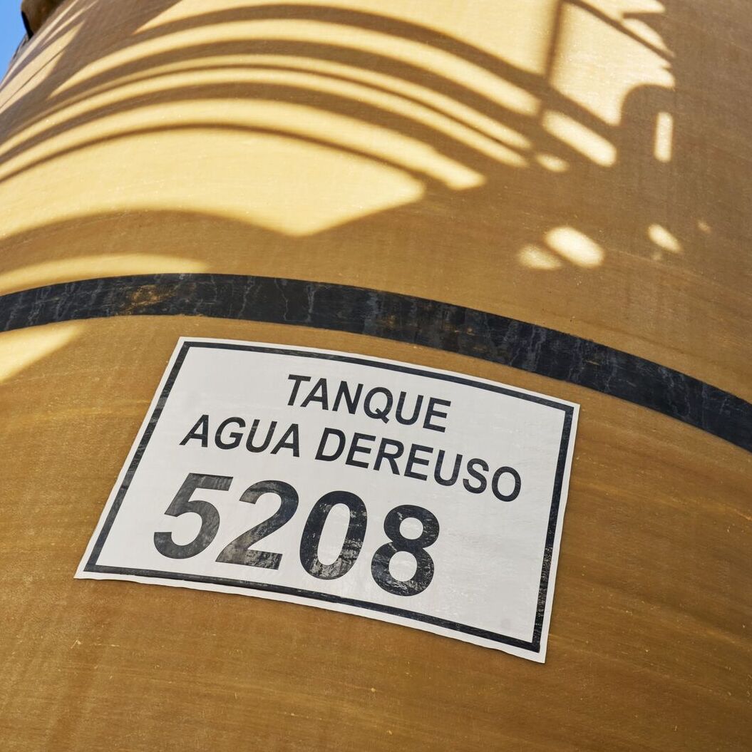 Close-up of yellow-orange water tank with black horizontal band and 'TANQUE AGUA DEREUSO 5208' label.