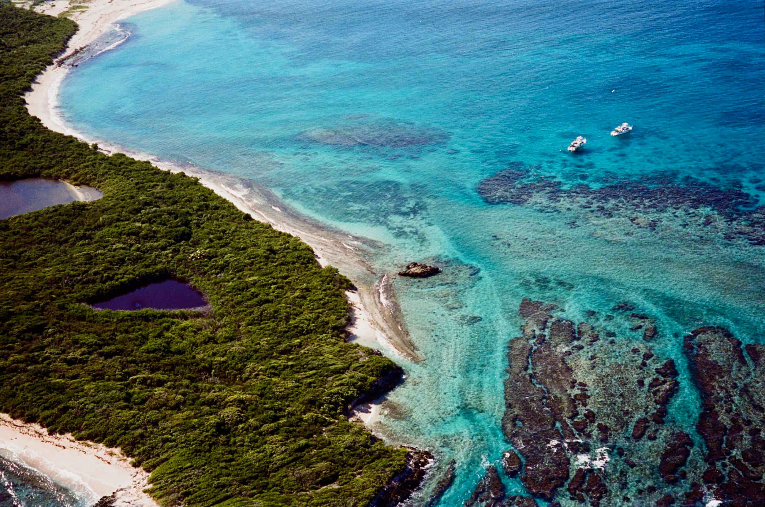Aerial view of tropical coastline with coral reefs, sandy beach, and two small white boats.