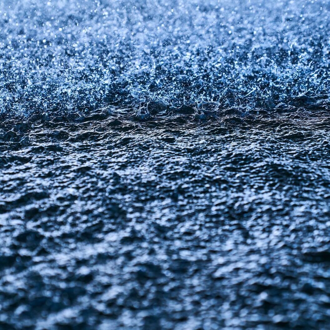 Close-up of water droplets splashing onto a dark blue water surface, creating dynamic texture.