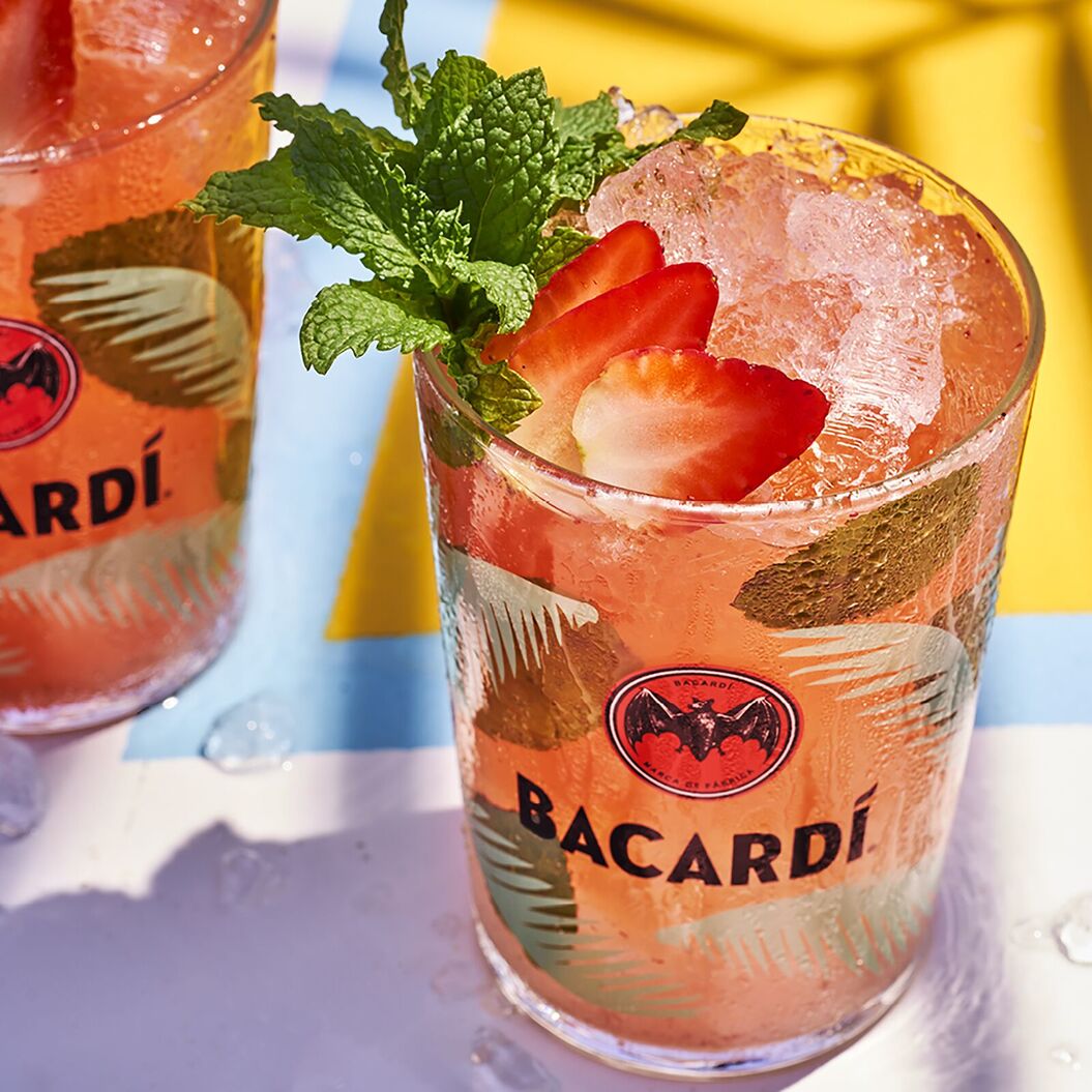 Two orange strawberry daiquiri cocktails in glasses with crushed ice, strawberries, and mint sprigs.