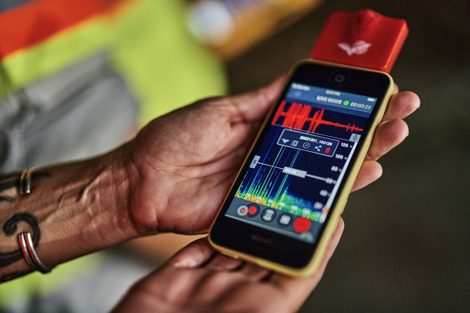 Hands holding a smartphone with a red bat detector, displaying a colorful graph on the screen.