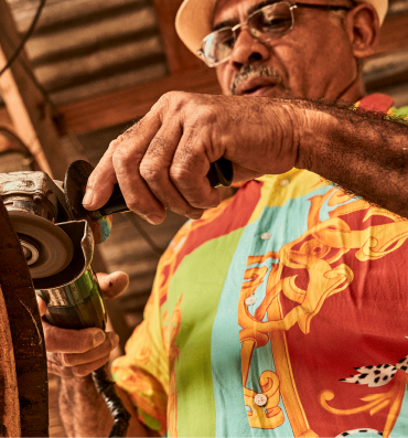 Person wearing a patterned shirt operating an angle grinder with focused intensity.