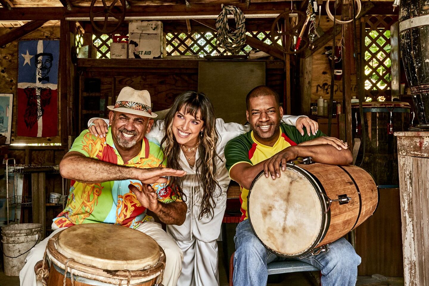 Three people gathered with drums in a rustic indoor setting, sharing a joyful musical moment.