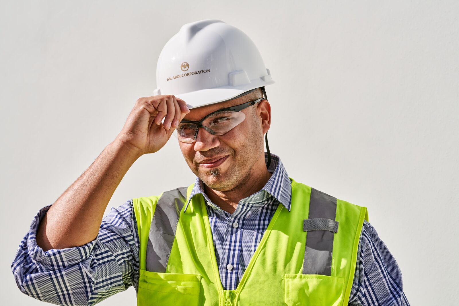 Worker wearing hard hat, safety glasses, and lime green safety vest, adjusting hat brim.