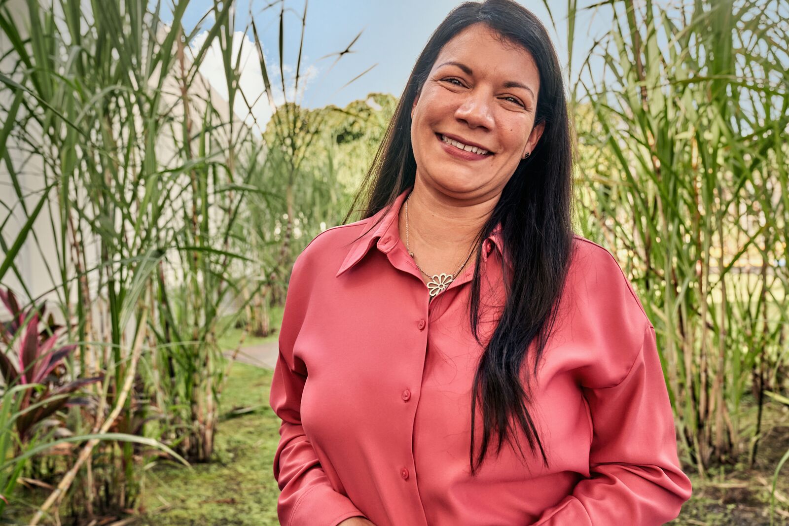 Person standing in tall sugarcane field wearing a coral-colored collared shirt.