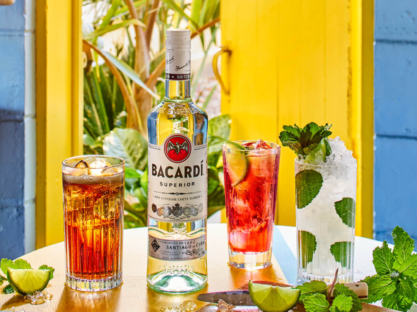 Bacardí Superior rum bottle with three cocktails, lime wedges, mint leaves.
