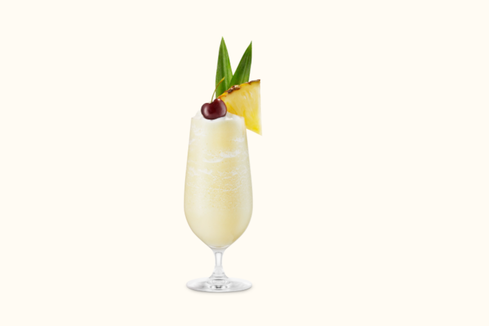 Creamy Piña Colada in a hurricane glass with pineapple wedge, dark cherry, and two green pineapple leaves.