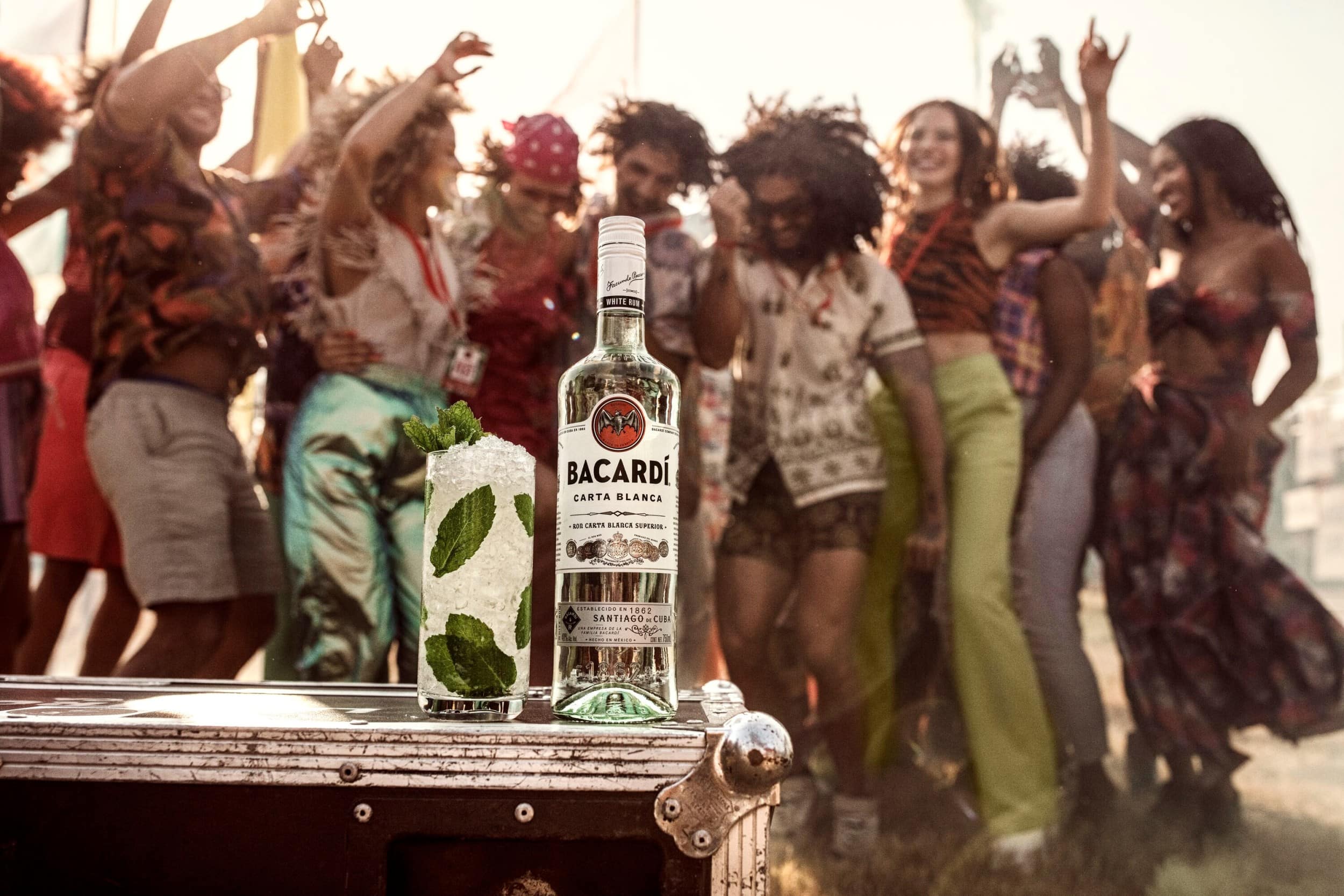 BACARDÍ Carta Blanca rum bottle next to a mojito cocktail with mint leaves, crushed ice.