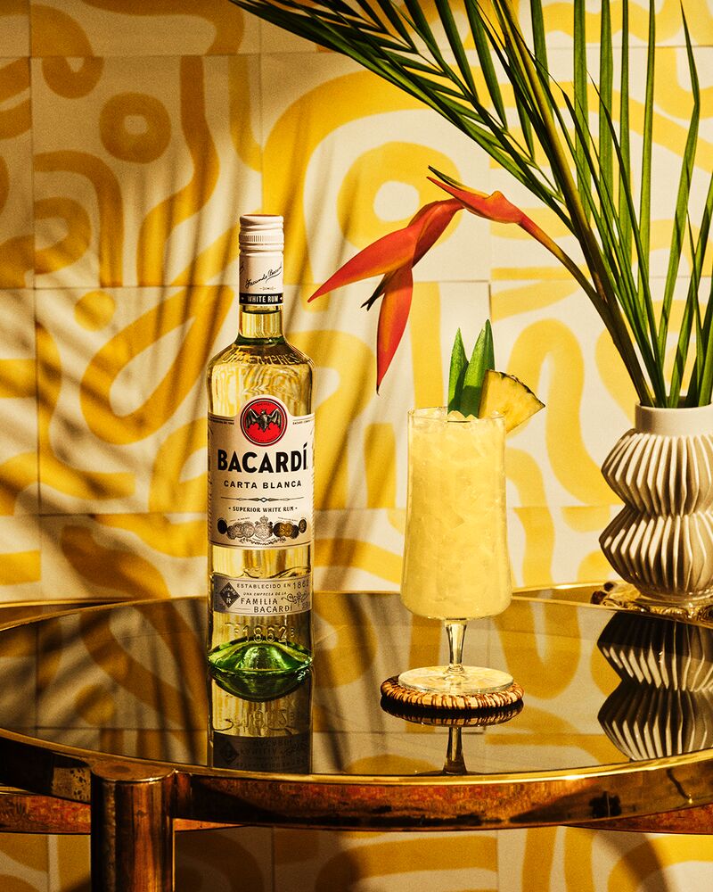 BACARDÍ Carta Blanca rum bottle next to a piña colada cocktail with pineapple garnish.