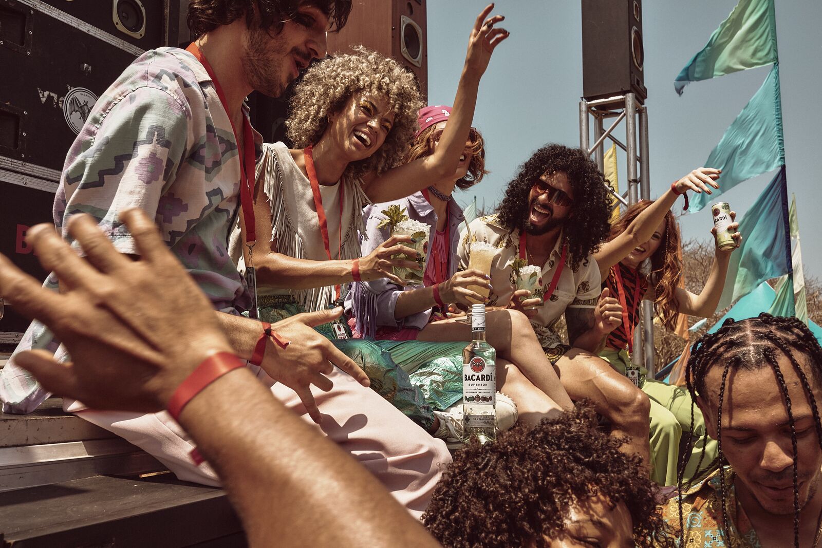 Group of friends at a festival with BACARDÍ rum bottle, holding cocktails, surrounded by flags.