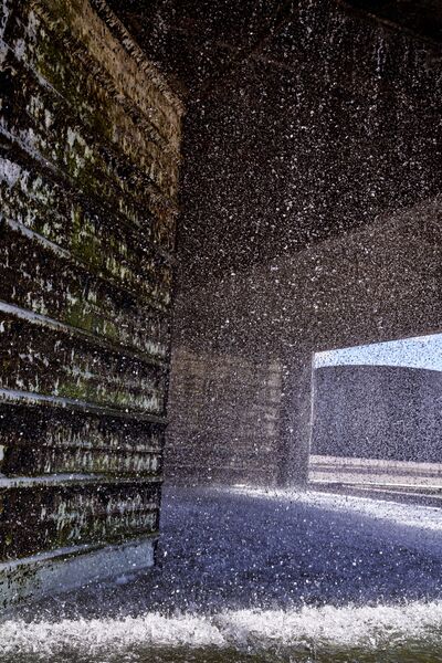 Dynamic close-up of water droplets spraying and splashing against dark, textured wall.