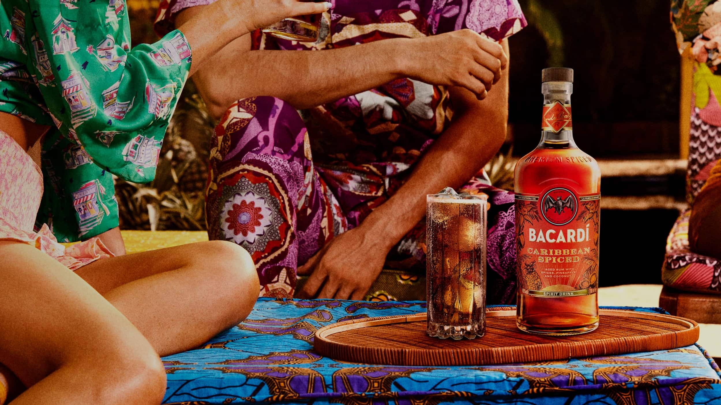 BACARDÍ Caribbean Spiced rum bottle and cocktail glass on a tray with two people seated nearby.