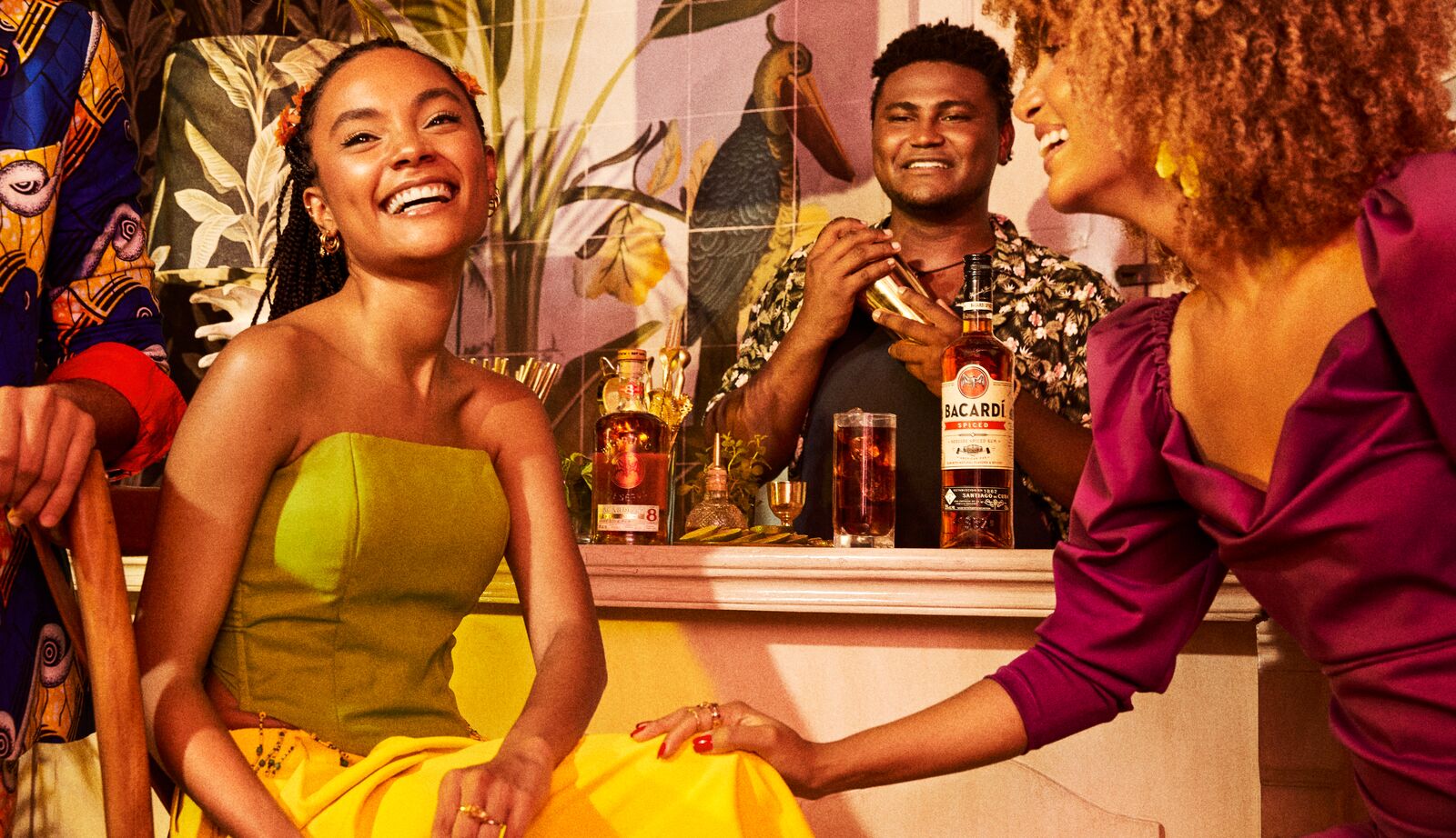 Three people interacting at a bar with a BACARDÍ Spiced rum bottle and cocktail shaker.