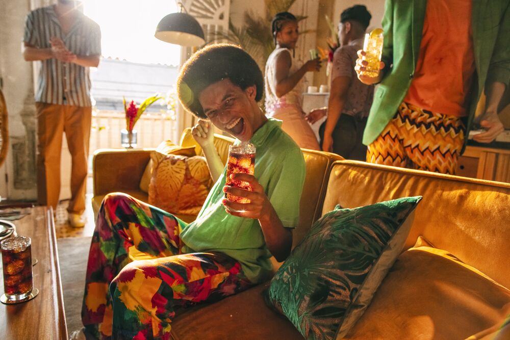 Person seated on a couch, holding a cocktail during an indoor social gathering.