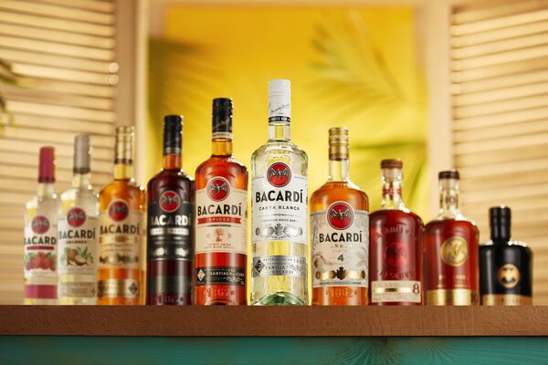 Collection of BACARDÍ rum bottles arranged on a wooden shelf with soft lighting.