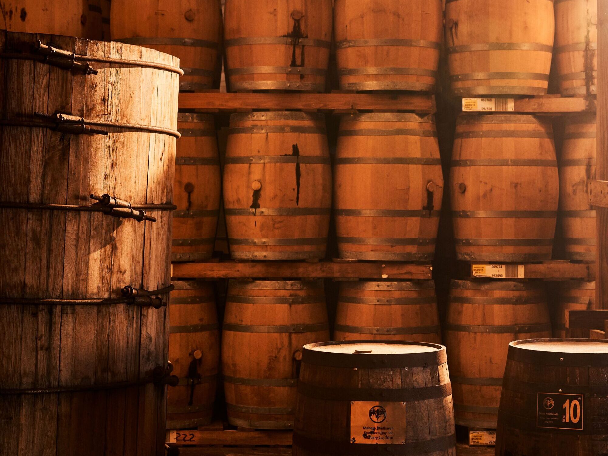 Dimly lit room filled with numerous wooden barrels stacked from floor to ceiling, with metal bands.