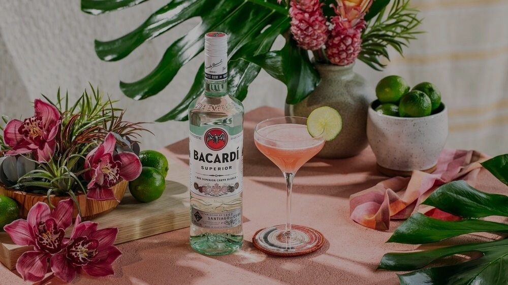 BACARDÍ Superior rum bottle next to a pink cocktail with lime slice and tropical flowers.