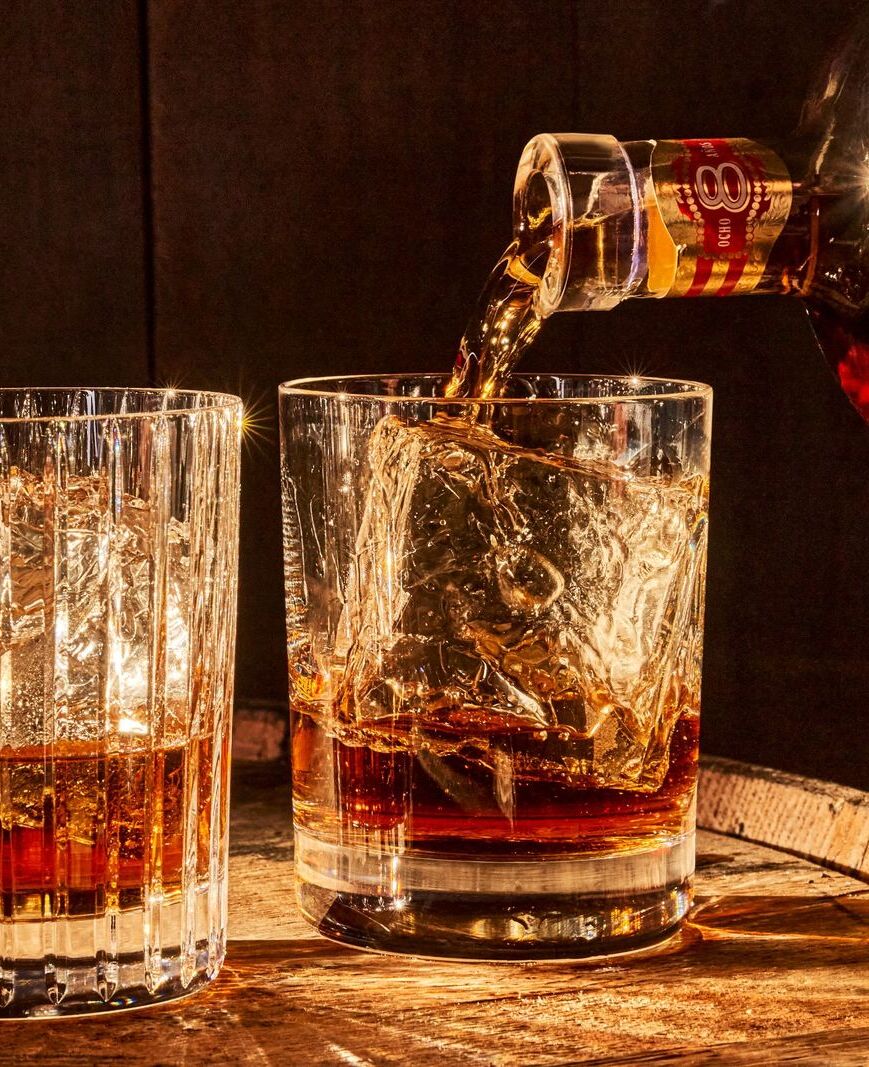 Dark amber rum being poured into a glass with large ice cubes, creating a liquid splash.