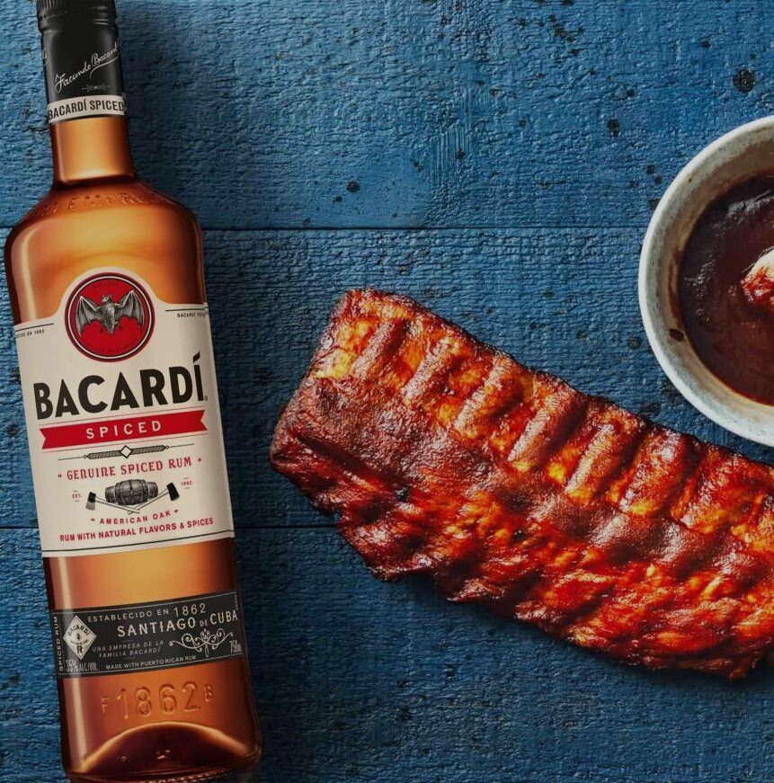 BACARDÍ Spiced rum bottle next to a rack of barbecued ribs and dark sauce.